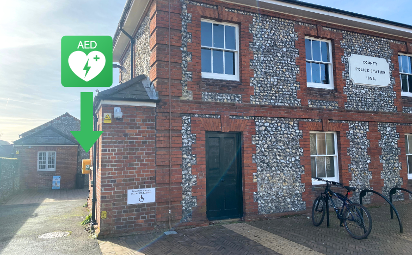Exterior brick and flint walls of Petersfield Museum and Art Gallery with big green arrow pointing to eastern wall where the defibrillator is located.