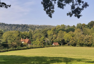 Looking out across a grassy field toward woodland and houses nestled in the hillside.