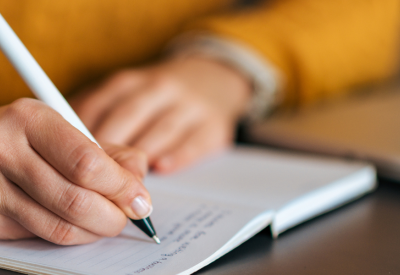 Author writing at a desk with pen and paper.