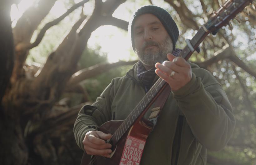 Alex Roberts playing his guitar in the forest.