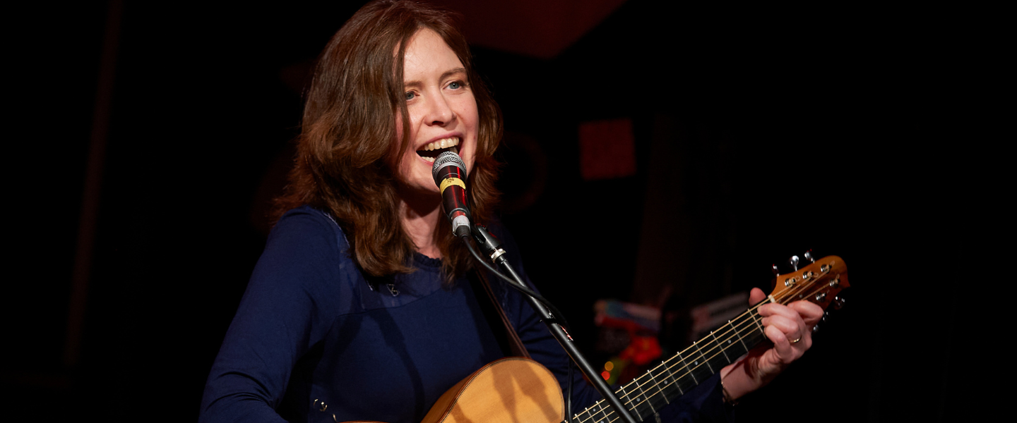 Singer Sarah McQuaid singing and playing the acoustic guitar