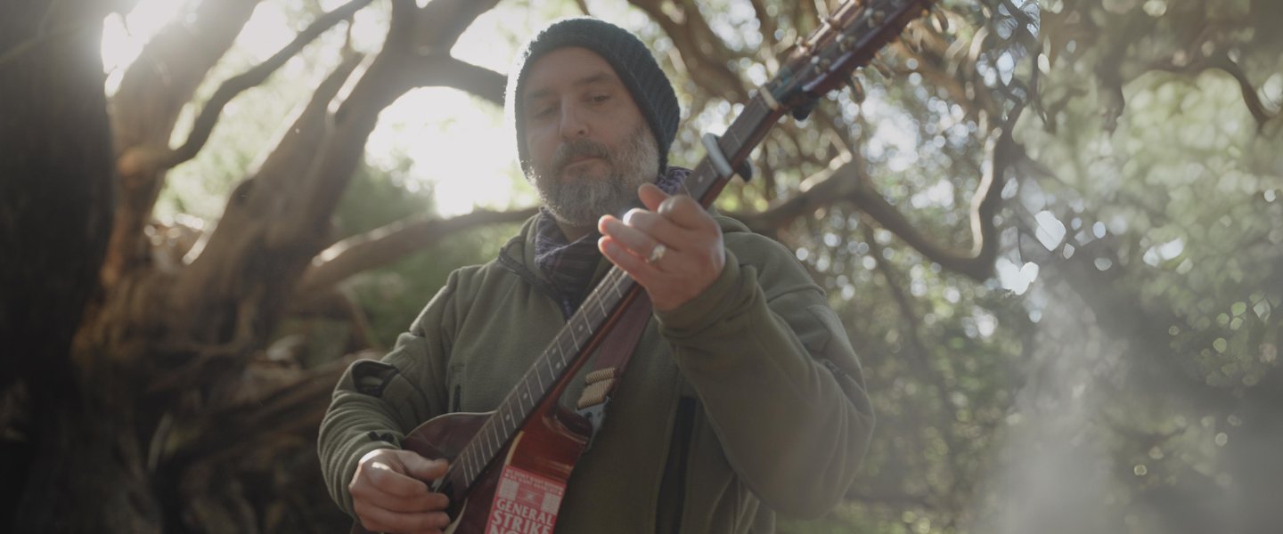 Alex Roberts playing his guitar in the forest.