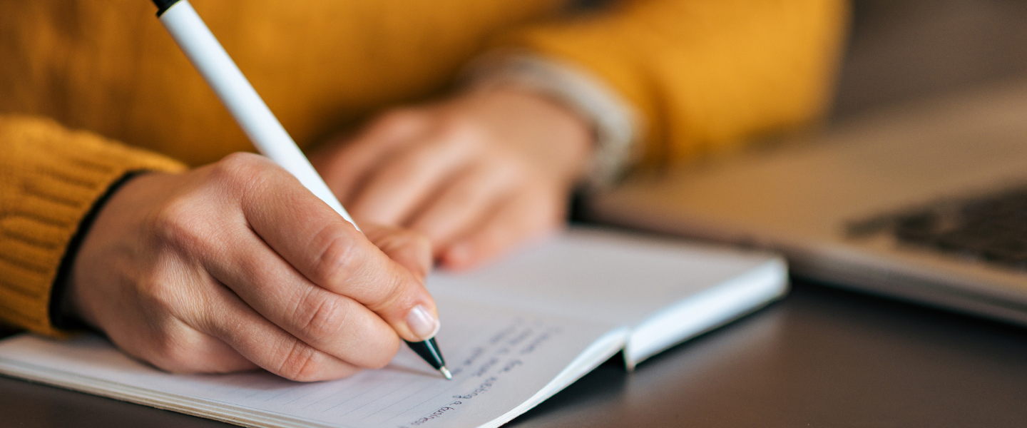 Author writing at a desk with pen and paper.